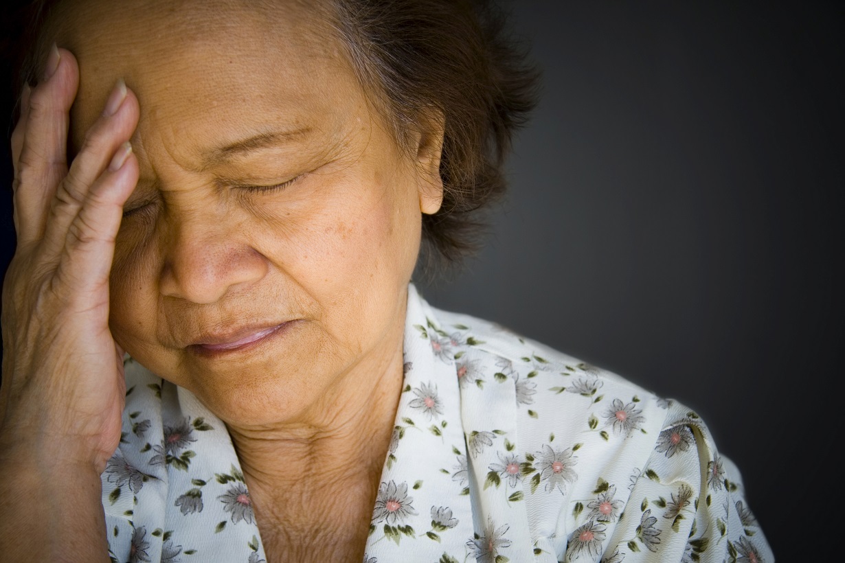 senior woman with closed eyes holds her hand to her head